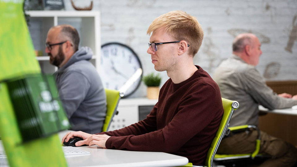 An image of three Nettl employees working on computers. There are two at a foreground table, with one person in the background.