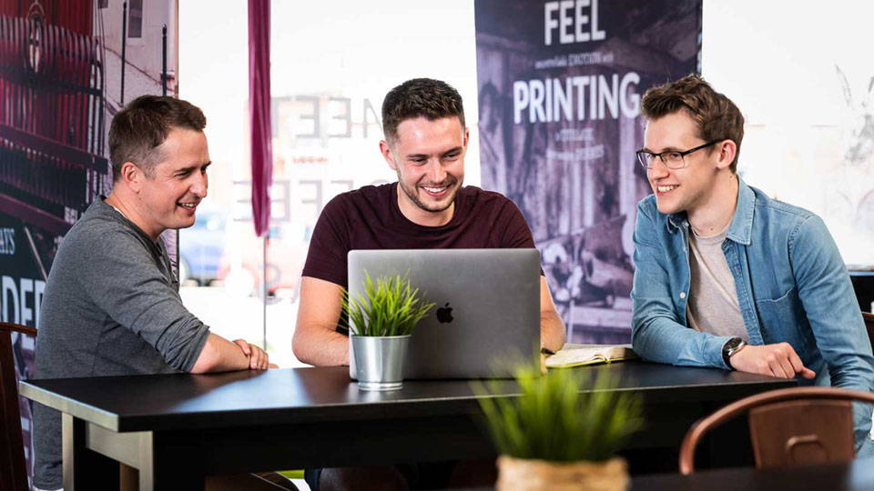 Three Nettl employees working through a design marketing project. They are huddled around a small table.
